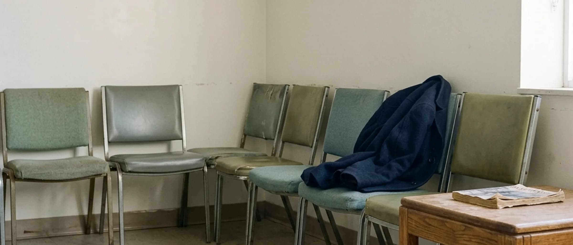 A row of plain clinic chairs along a wall in a quiet waiting room.